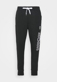 Svarta sweatpants i mjukt tyg, med en vit dragsko, ribbade muddar och "KORS"-logotypen tryckt i vitt längs vänster ben.
