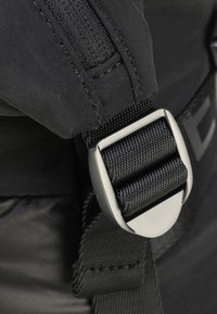 Sort nylonrem med en mat-sølv spænde. Har tekstureret stof og et Velcro-afsnit, der understreger holdbarhed og funktionalitet.