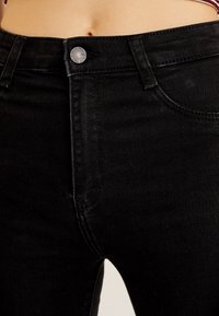 Jeans negros de talle alto con una textura lisa, que presentan un cierre de botón plateado, un diseño clásico de cinco bolsillos y detalles de costura mínimos.