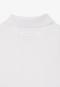 Vue arrière d'un col de chemise blanc avec une petite étiquette de marque rectangulaire cousue sous la bande du col.
