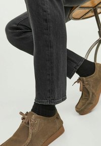 Pantalones de mezclilla gris con un corte ajustado, combinados con zapatos de ante marrón con cordones. Medias negras son visibles por encima de los zapatos.