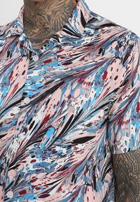 Koszula z krótkim rękawem z wielokolorowym abstrakcyjnym wzorem w różowe, niebieskie i czarne kolory. Wykonana z lekkiego materiału, z kołnierzykiem na guziki.