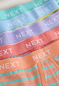Sous-vêtements empilés de couleur pastel avec larges bandes élastiques blanches portant la mention « NEXT », comprenant des motifs unis et rayés.