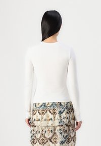 Cămașă albă cu mâneci lungi, având un decolteu rotund, asociată cu o fustă texturată, cu un model în nuanțe de crem, albastru și maro.
