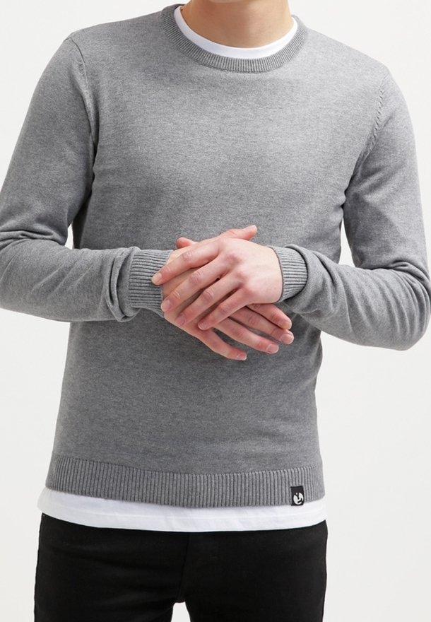 Grijze gebreide trui met een ronde hals, geribde manchetten en onderkant. Heeft een gelaagd wit shirt eronder en een klein logo aan de onderkant.