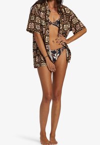 Czarna koszula z kolorowymi wzorami kwiatowymi i geometrycznymi, zestawiona z czarnym bikini z kwiatowym wzorem, prezentująca luźny fason.
