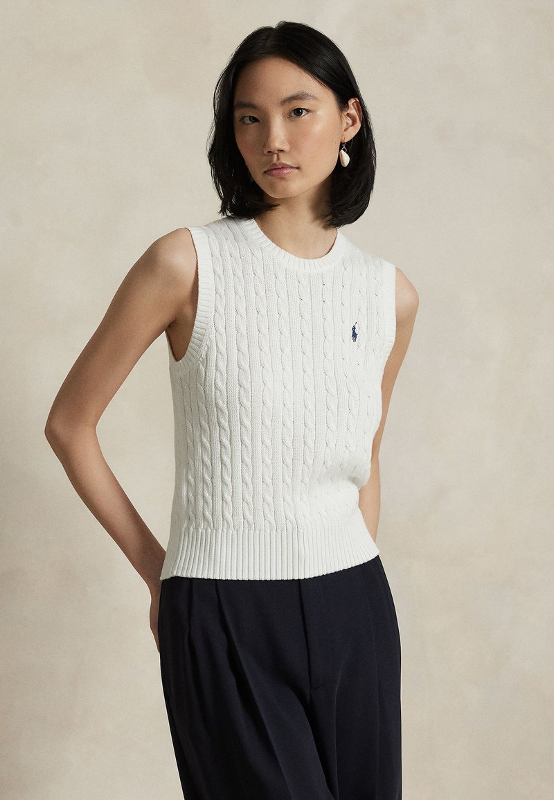 Balts trikotāžas veste bez piedurknēm ar ribveida apakšmalu. Uz krūškurvja ir neliels zils logotips, un veste ir ar gludu, fakturētu dizainu.