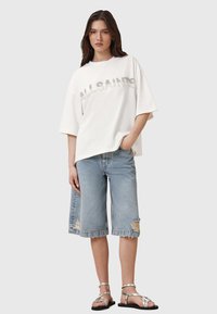 T-shirt bianca oversize a maniche corte con "ALLSAINTS" in strass, abbinata a pantaloni corti in denim chiaro strappati e sandali argento.