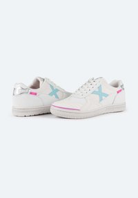 Zapatillas blancas con acentos en azul claro, parte superior de cuero texturizado, detalles rosas y una lengüeta trasera plateada. Cuentan con una suela de goma y cierre de cordones.