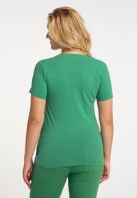 Grön bomulls T-shirt med korta ärmar och rund halsringning. Tyget är glatt med en figurnära passform och har sidoflikar i nederkant.