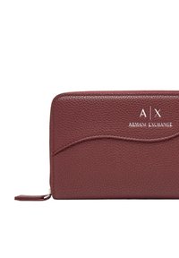 Portafoglio in pelle borgogna con finitura testurizzata, caratterizzato da un dettaglio a cucitura curva e logo "Armani Exchange" in bianco in rilievo. Chiusura con zip.