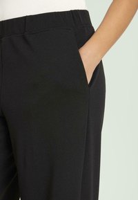 Pantalones con cintura elástica negra y bolsillos laterales; textura suave y diseño ajustado para una apariencia ceñida.