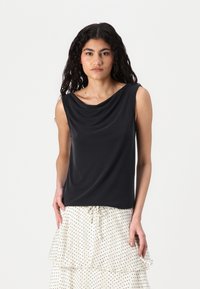 Haut sans manches noir avec un décolleté drapé, en tissu doux et avec une coupe décontractée, accompagné d'une jupe crème ornée de pois noirs.