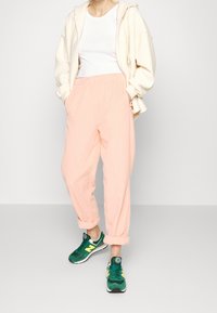 Světle růžové, texturované kalhoty s elastickým pasem, zkombinované s bílým tílkem a krémovou mikinou. Zelené tenisky s žlutými akcenty.