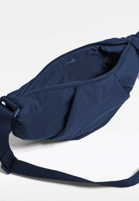 Sac bandoulière en tissu bleu marine avec fermeture éclair, texture rembourrée et bandoulière réglable. L'intérieur est doté d'une petite poche zippée.