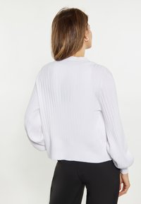 Weißer gerippter Pullover mit langen, luftigen Ärmeln und abgeschnittenem Saum. Glatte Textur, minimalistisches Design ohne sichtbare Beschläge oder Akzente.