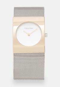 Montre à bracelet en maille argentée avec un boîtier rectangulaire en ton or et un cadran blanc. Présente un design minimaliste et des aiguilles dorées non marquées pour l'indication de l'heure.