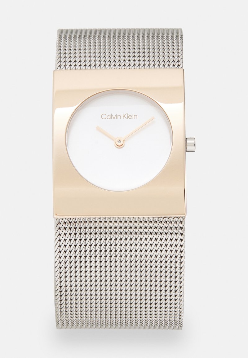 Montre à bracelet en maille argentée avec un boîtier rectangulaire en ton or et un cadran blanc. Présente un design minimaliste et des aiguilles dorées non marquées pour l'indication de l'heure.