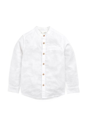Chemise blanche à manches longues avec des boutons marron, un col mao et une petite poche poitrine sur un fond uni.