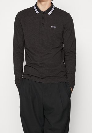 Person trägt ein dunkelgraues langärmeliges Poloshirt mit weißem gestreiftem Kragen und weißem "BOSS"-Logo, kombiniert mit locker sitzenden schwarzen Hosen.