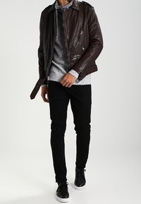 Bruine leren jas met ritszakken, grijze gebreide trui, zwarte jeans en zwarte sneakers, wat een gelaagde casual uitstraling creëert.