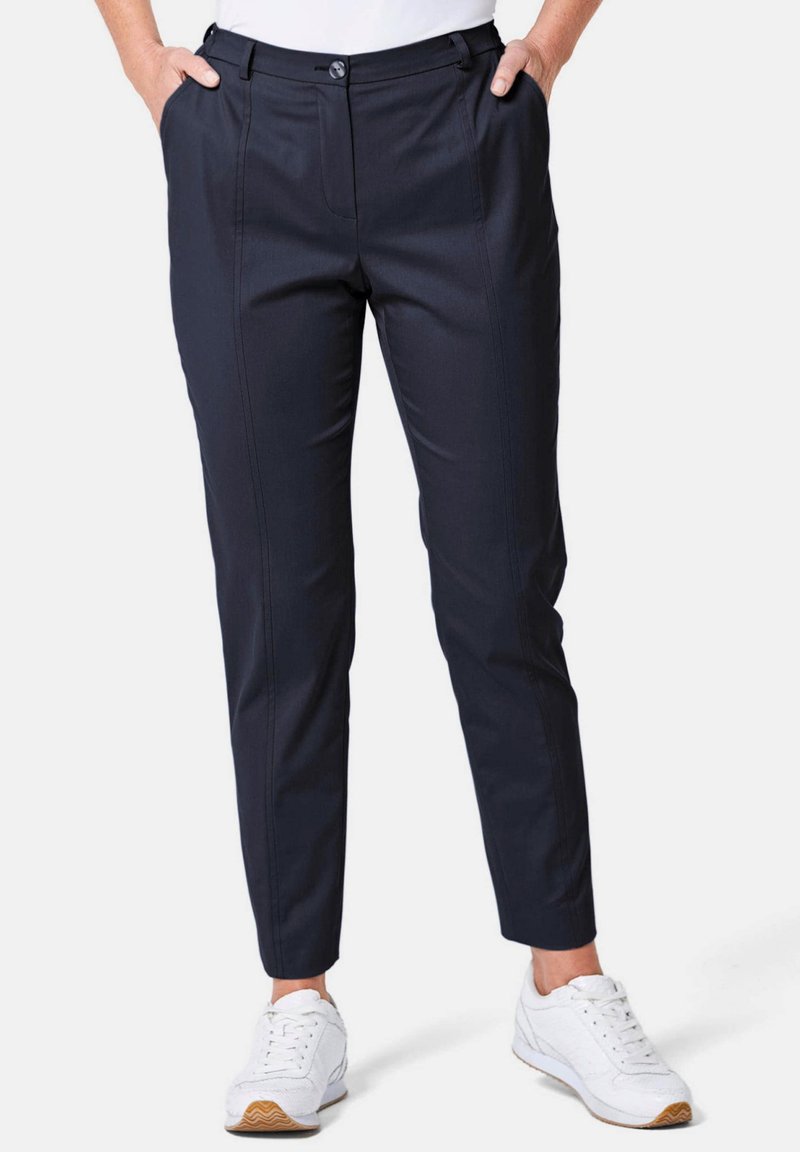 Pantalons tailleurs bleu marine avec une coupe plate, poches latérales et jambes fuselées, fabriqués à partir de tissu lisse. Assortis à des baskets blanches.