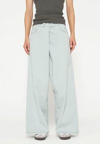 Jeans a gamba larga di colore azzurro chiaro con vita alta, realizzati in denim, dotati di tasche frontali e cuciture a contrasto. Abbinati a sneakers grigie.