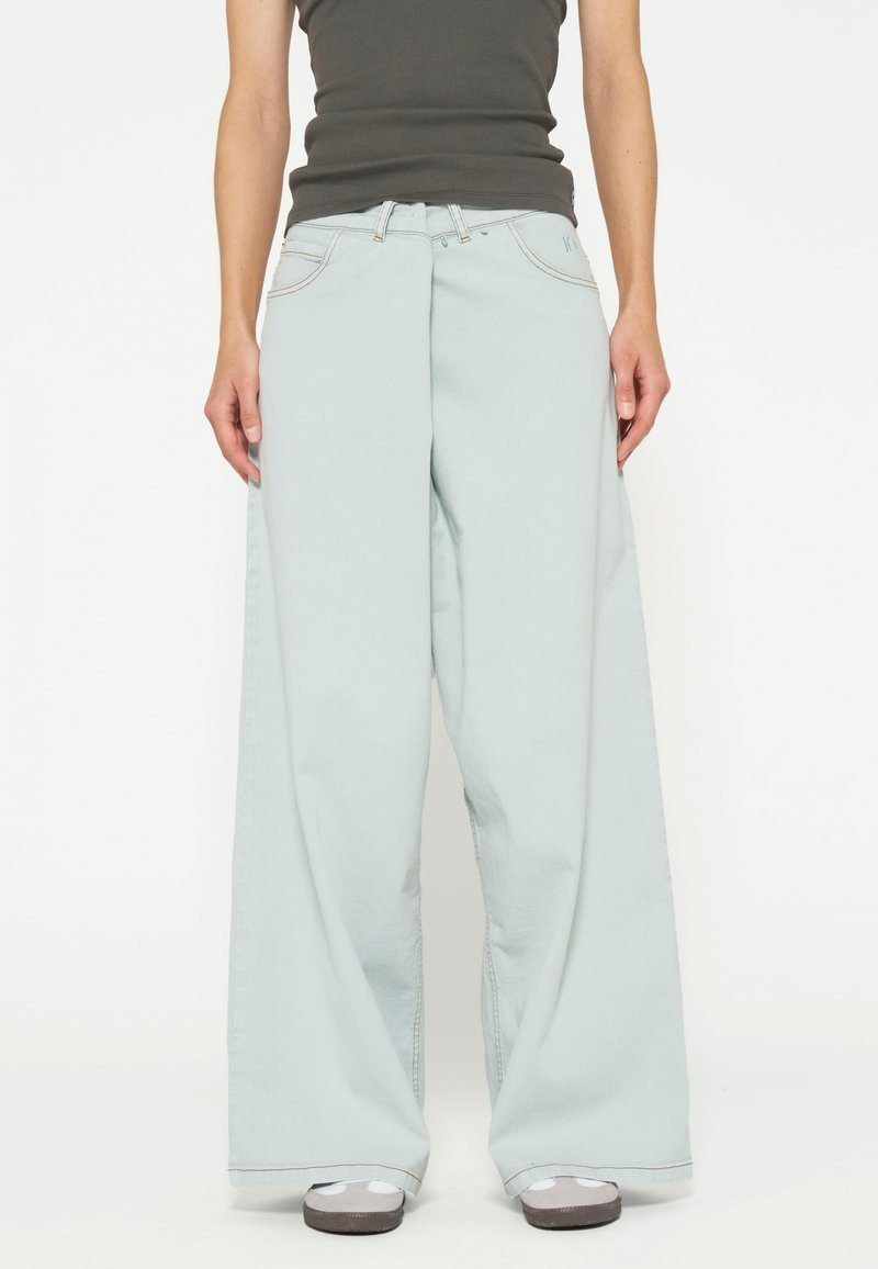 Jeans a gamba larga di colore azzurro chiaro con vita alta, realizzati in denim, dotati di tasche frontali e cuciture a contrasto. Abbinati a sneakers grigie.