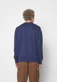Sudadera azul marino con cuello redondo, puños y dobladillo acanalados, con una textura suave y un ajuste relajado. Pantalones cargo marrones abajo.