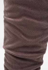 Gros plan d’un tissu brun doux et texturé avec de légers plis et des ombres suggérant une surface de matériau pelucheux.