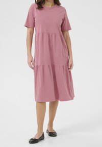 Robe rose à manches courtes avec étages, confectionnée en tissu doux, dotée d'un col rond et d'une coupe décontractée. Associée à des chaussures plates noires.