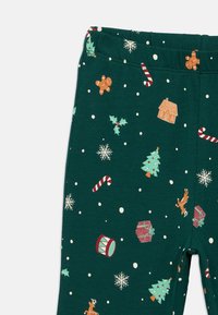 Leggings de tecido verde com padrões temáticos de férias: homens de gengibre, árvores de Natal, bengalas de doces, flocos de neve e caixas de presentes.
