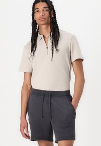 Beige ribbet polo-shirt med halv-zip krave, parret med mørkegrå strukturerede shorts med elastisk talje og sidelommer.
