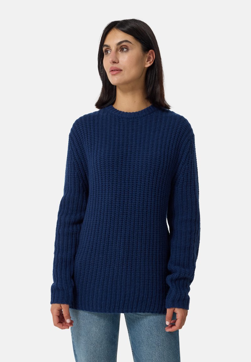 Maglione lavorato a maglia blu navy con un motivo testurizzato, maniche lunghe e scollo rotondo, abbinato a jeans chiari.