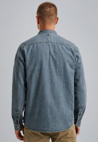 Jasnoniebieska koszula dżinsowa z kołnierzykiem zapinanym na guziki, długimi rękawami i kieszenią na piersi. Posiada przeszywane akcenty oraz lekko zaokrąglony dół.