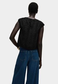 Top negro corto sin mangas con patrón texturizado en zigzag, combinado con unos pantalones vaqueros de tiro alto y pierna ancha en azul, que cuentan con bolsillos traseros.