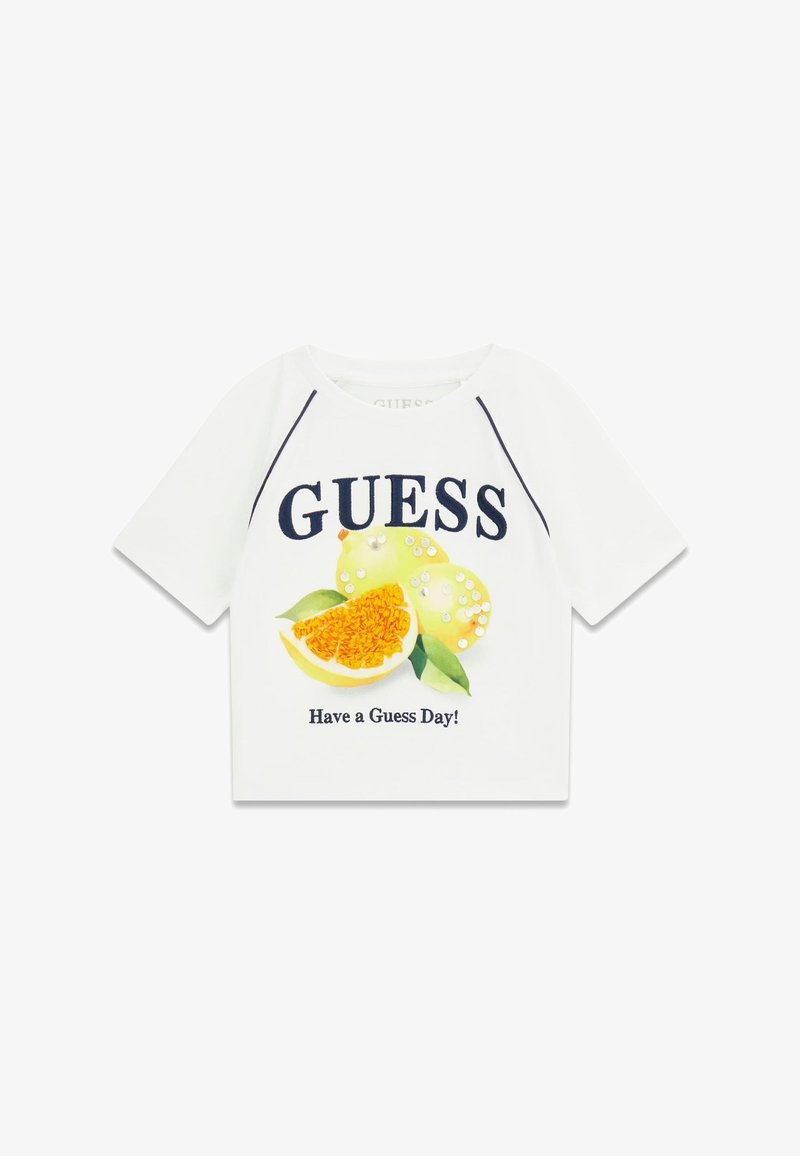 Λευκό πουκάμισο με κοντά μανίκια, με τη λέξη "GUESS" σε μεγάλους χαρακτήρες, ένα γραφικό εσπεριδοειδούς φρούτου με παγιέτες και το κείμενο "Have a Guess Day!" από κάτω.