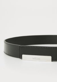 Must mustriba nahkavööd, millel on sile viimistlus, ja hõbedane ristkülikukujuline pandla, millel on graveering "Moschino". Lihtne, minimalistlik disain.