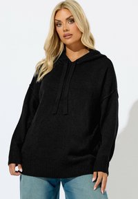 Felpa nera con vestibilità rilassata, polsini e orlo a coste, cordini regolabili e tessuto morbido e testurizzato. Abbinata a jeans azzurri chiari.