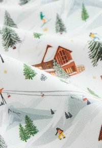 Mønstret stof med et sneklædt landskab med træer, skitrekkere, hytter og skiløbere. Farverne inkluderer hvid, grøn, brun og orange.