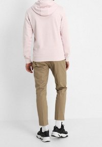 Hellrosa Kapuzenpullover mit Kordelzug, kombiniert mit beige zulaufenden Hosen und schwarzen Turnschuhen. Mit gerippten Bündchen an Ärmeln und Saum.