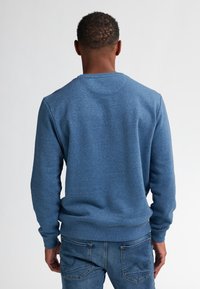 Blauwe sweatshirt met een ronde hals, ribgebreide manchetten en onderrand, gemaakt van zachte, textuurstof. Draagt het met blauwe jeans, gezien van achter.
