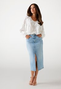 Blusa bianca ricamata con motivi floreali e maniche a palloncino abbinata a una gonna di jeans a vita alta con uno spacco frontale e un lavaggio azzurro chiaro.