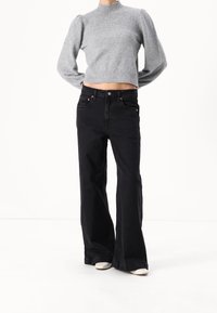 Grijze, korte, gebreide trui met pofmouwen, gecombineerd met zwarte, high-waisted, wijde jeans en beige hakken.