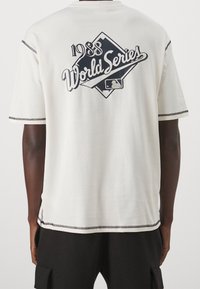 Bílý bavlněný tričko s černým grafickým designem "1988 World Series", tvar diamantu, krátké rukávy, kontrastní švy podél okrajů.