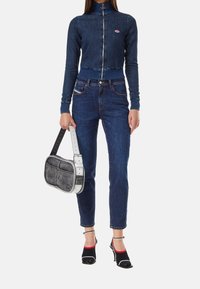 Jeansjacka med hög krage, kort passform och dragkedja. Mörkblå jeans med slim fit. Vit och grå handväska med en strukturerad design.