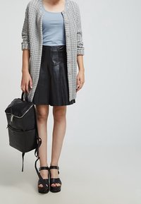 Gray textured cardigan, light blue shirt, black leather skirt, black platform sandals, and a black backpack with silver hardware.