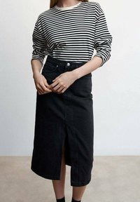 Jupe en denim noir avec fente sur le devant, associée à une chemise à manches longues rayée noir et blanc. Le tissu semble robuste et texturé.