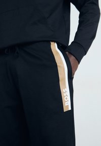 Sorte joggebukser med gull- og hvite side-striper, med "BOSS" branding. Mykt stoff, elastisk midjebånd og sidelommer.