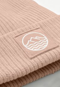Pink ribbed beanie featuring a square patch with a white mountain and wave graphic. Soft texture with visible knit pattern.
